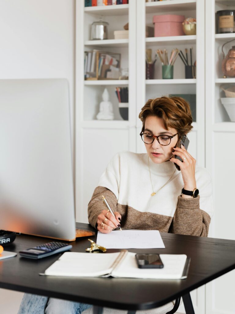 pexels-photo-4491469-4491469 Focused businesswoman in modern office multitasking efficiently while on a phone call.