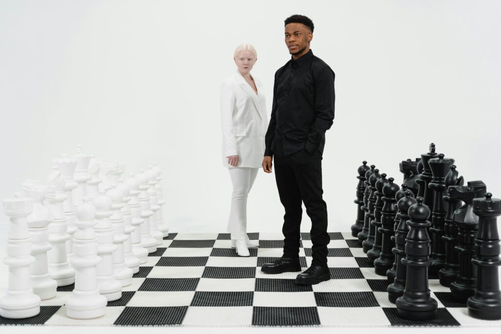 Two individuals stand on a life-sized chessboard engaged in strategic thinking.